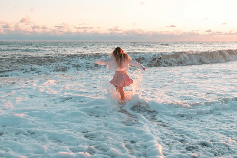 a girl in a pink dress splashes on the beach