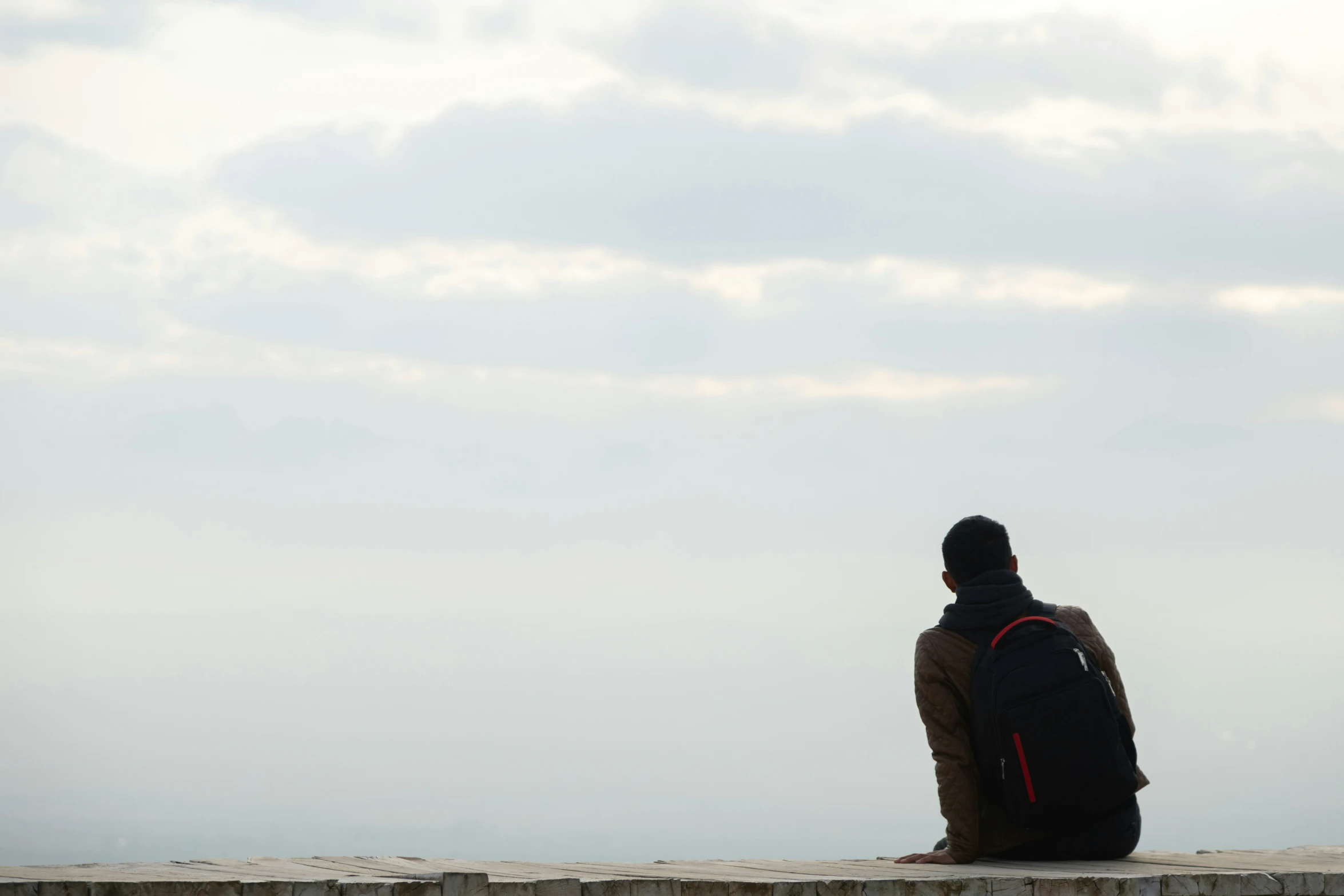 a person with backpack sitting on a stone wall watching the water