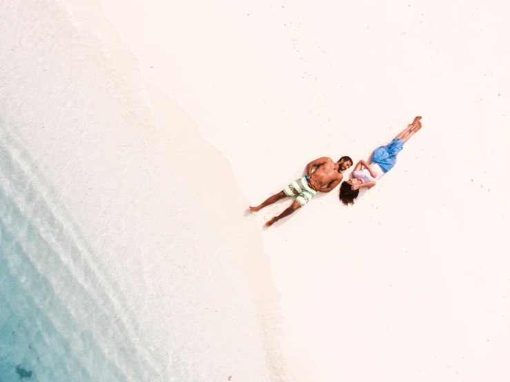 two people laying on the beach with no one wearing a hat