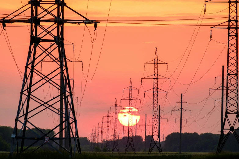 an orange sky at sunset with the sun setting behind electric power lines