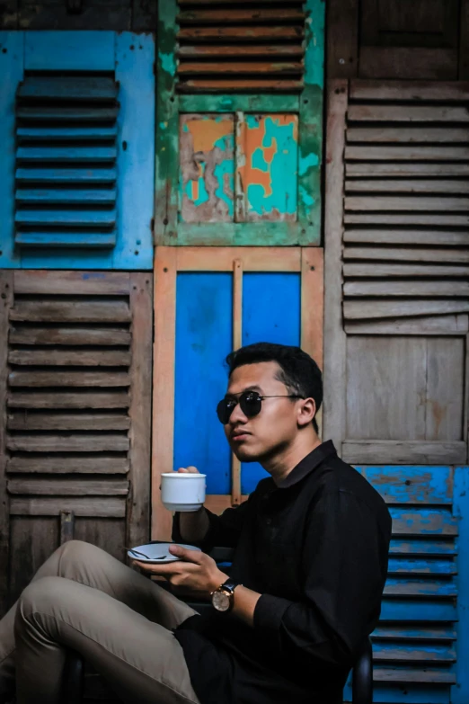 a man with sunglasses is sitting down reading and drinking coffee