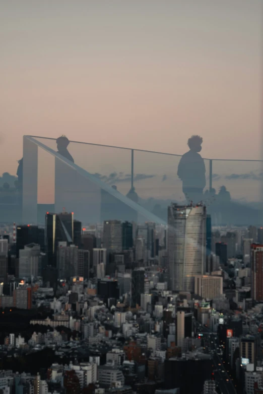 two people are standing on the edge of a tall building, overlooking the cityscape and mountains