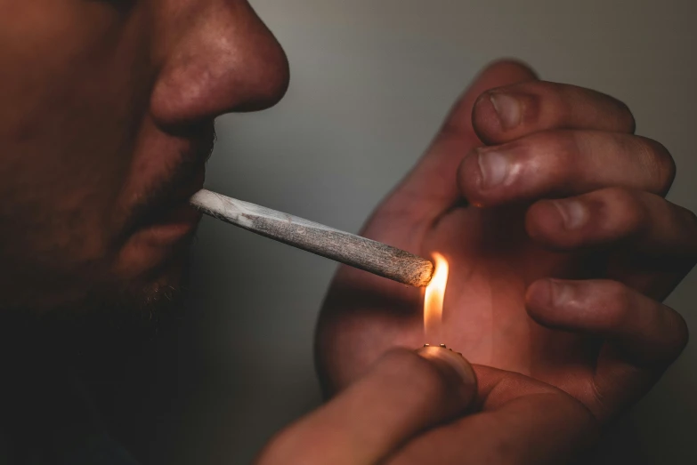 man lighting cigarette with one cigarette tip in his mouth