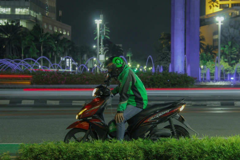 a man in a green and black hoodie rides his red motorcycle