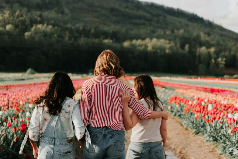 three people are walking in a field of flowers