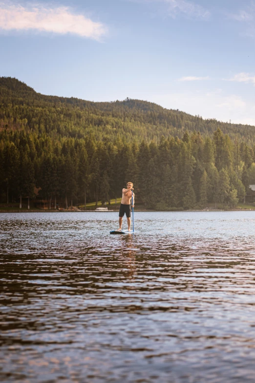 man paddleboarding on water in front of green mountain