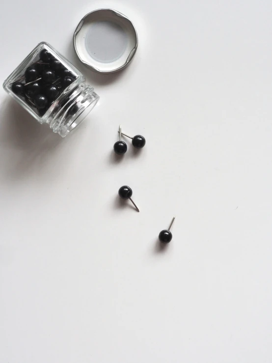 a pair of small black pearls next to a container of earrings