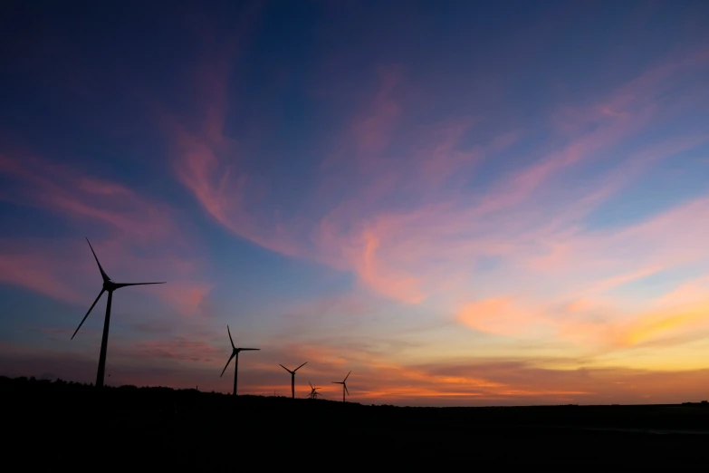 three windmills on a hill near a sunset