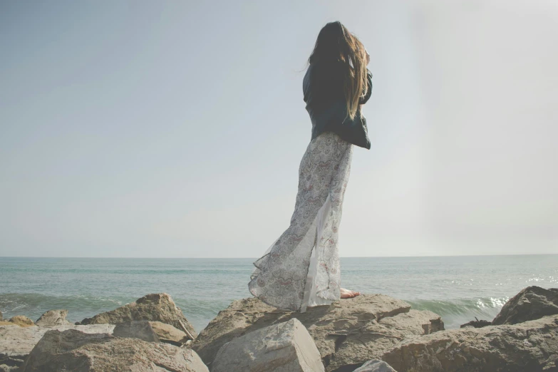 a woman stands at the edge of some rocks overlooking the ocean