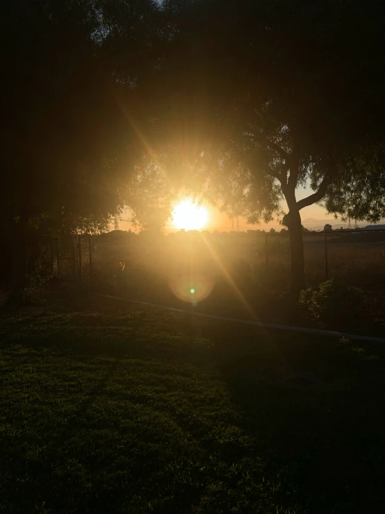 the sun sets in a field behind a fence