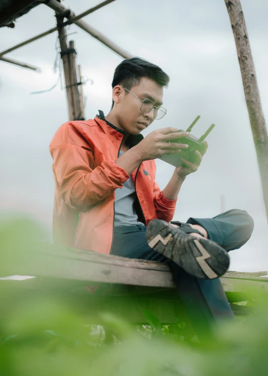 man in orange jacket sitting on ground holding cellphone