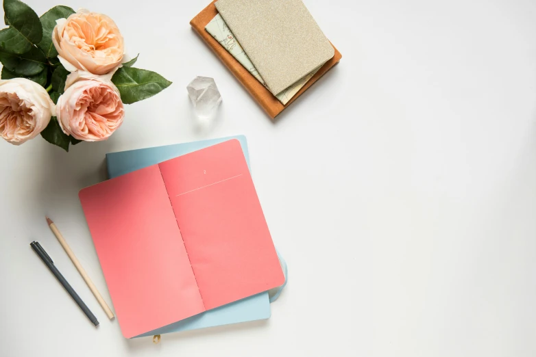 some pens, notebooks and flowers are arranged on a table