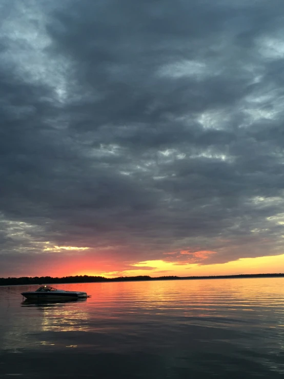 a boat floating across a lake under a cloudy sky