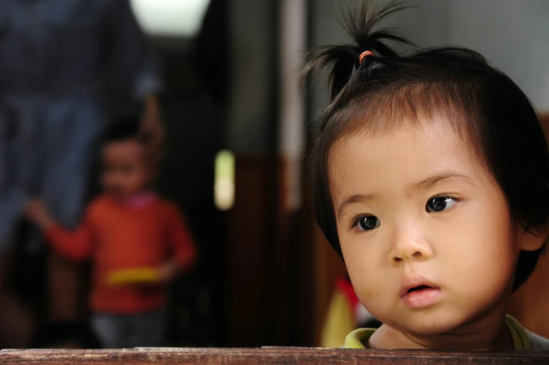 a small child with pigtails stands by a wooden table