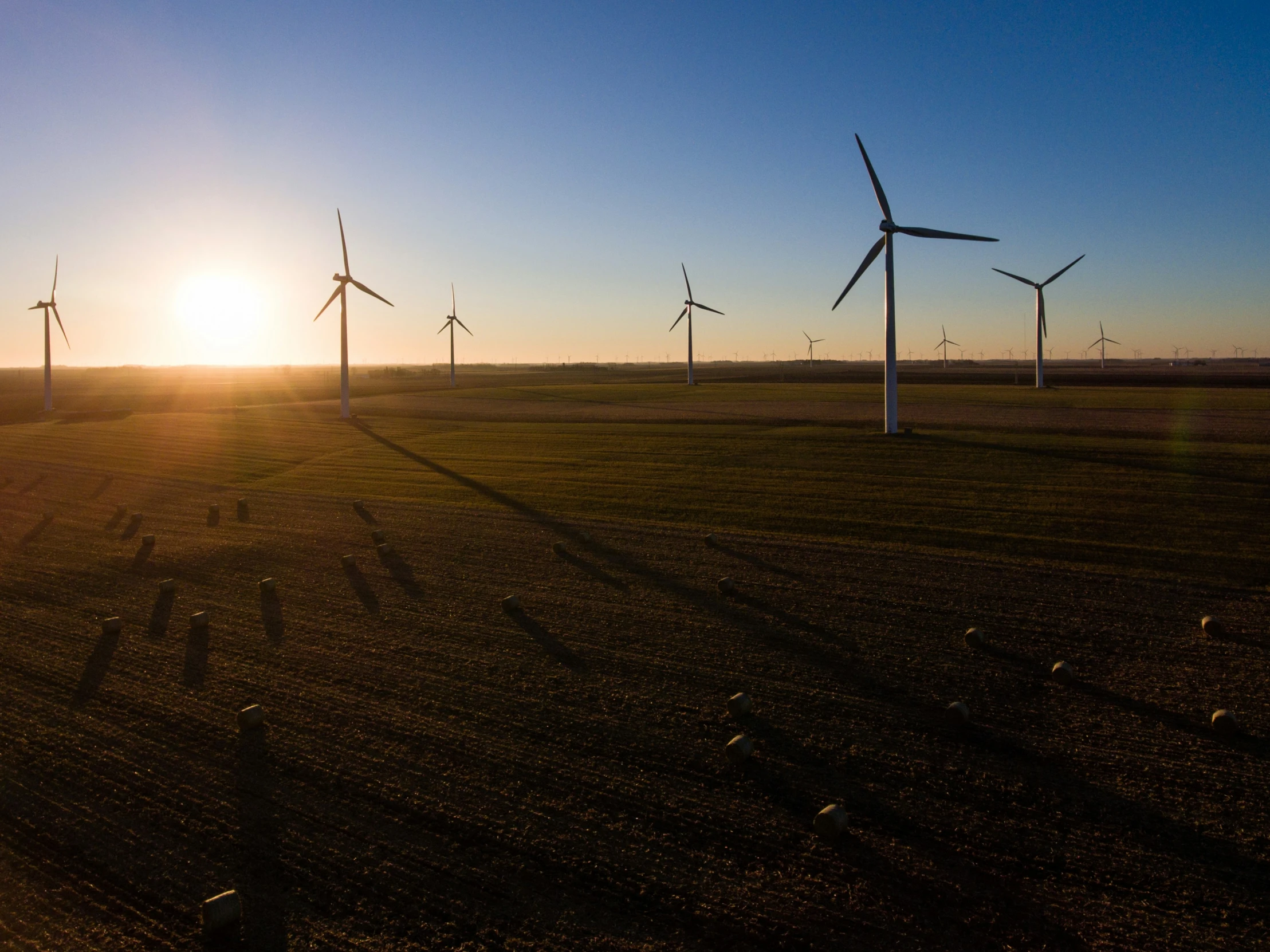 the sun shines through a cloudy sky behind a windmill field