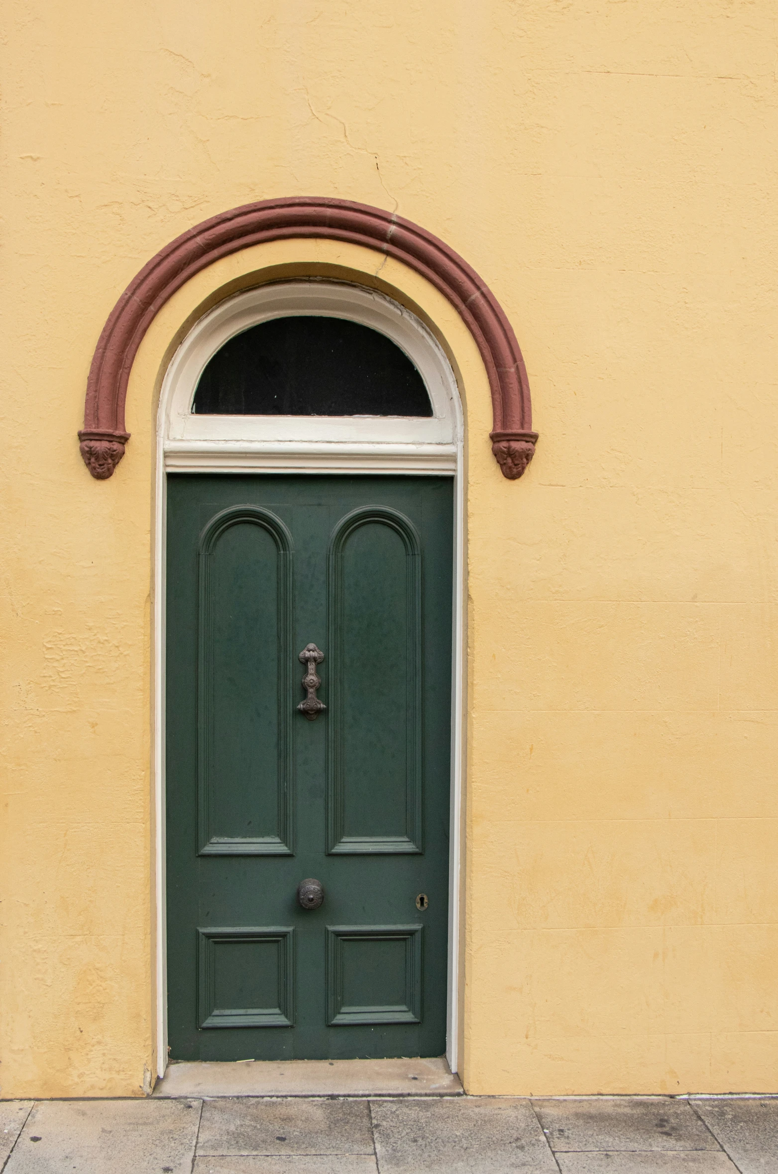 green door next to yellow wall with arched window