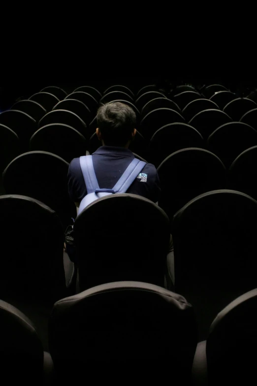 man sitting on empty chair in dark auditorium with lights