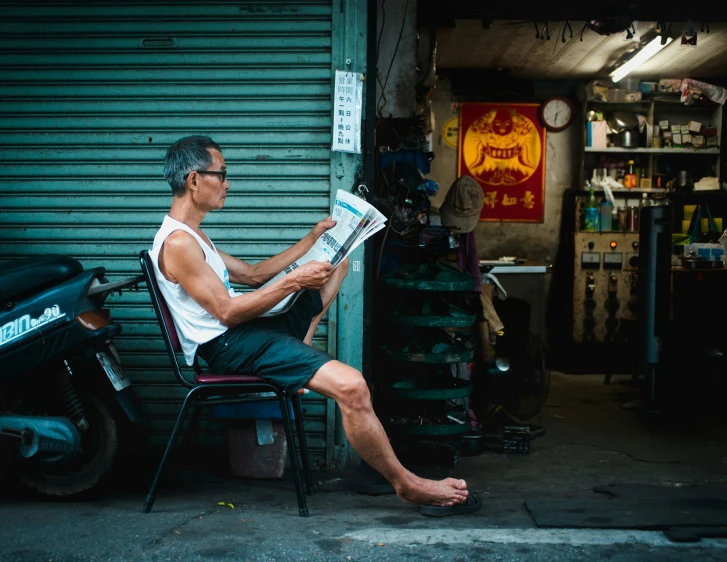 man reading a newspaper near a motorcycle