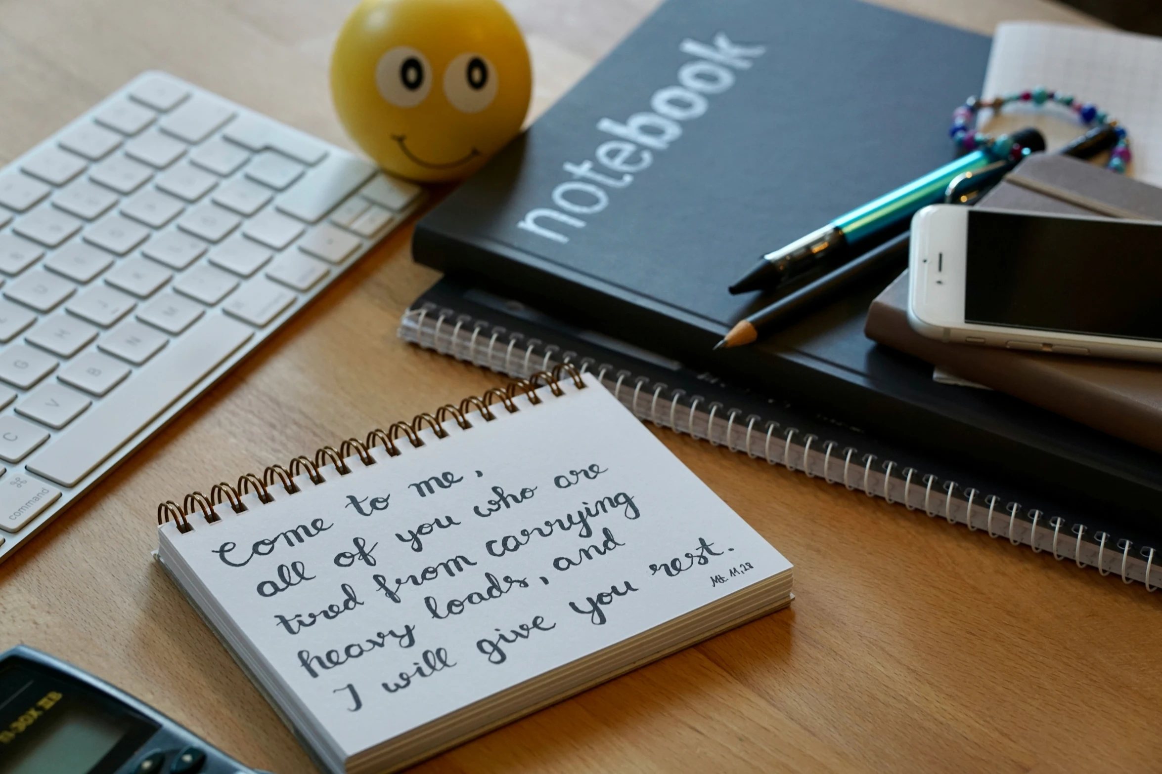 notebooks, a keyboard and a mobile phone sitting on top of a desk