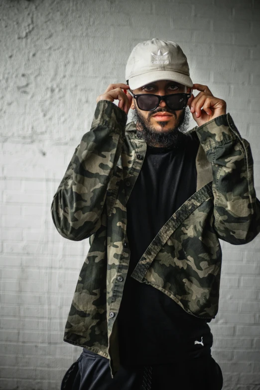 a man poses for a picture wearing a cap, jacket and sunglasses