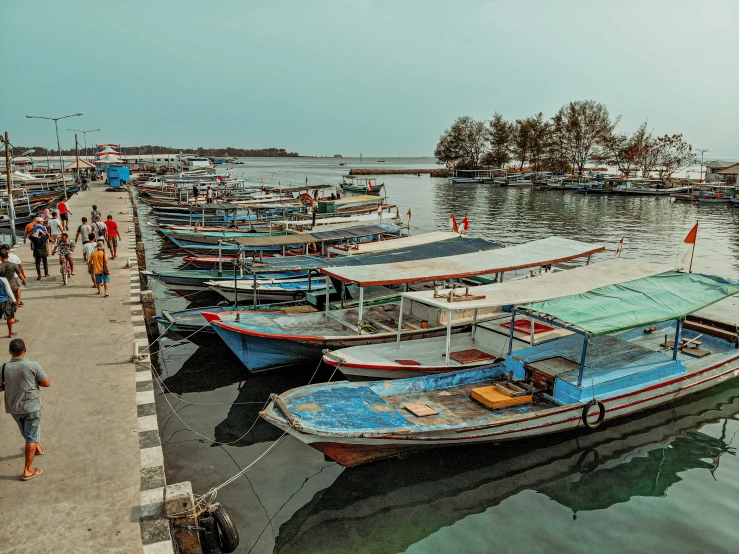 boats docked at the pier with people walking by