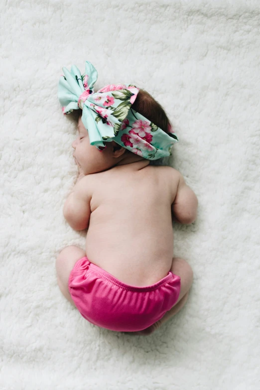 a baby sleeping on white carpet with a headband on