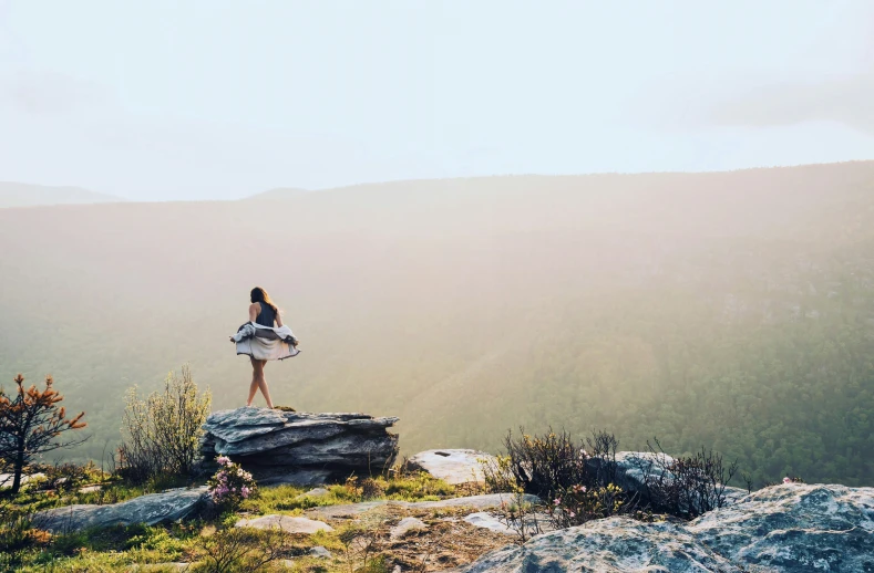 a woman standing on a rock with mountains behind her