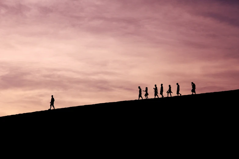 five people walking along a hill at sunset