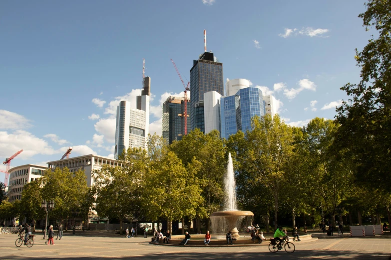 people walk around a fountain in the center of a park