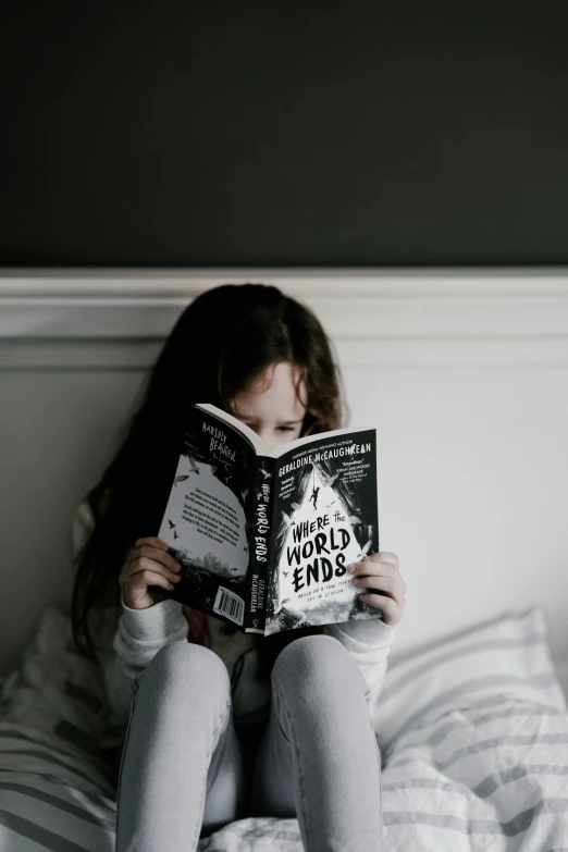 a girl is sitting on a bed reading a book