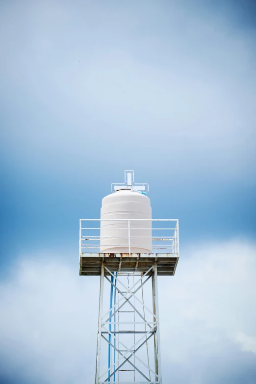 a water tower against a cloudy sky with a single white cylindrical structure