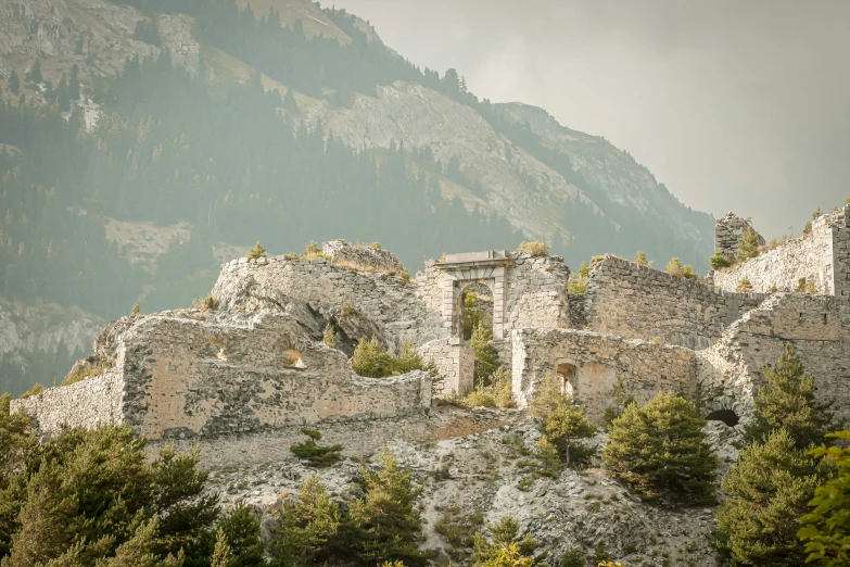 a stone building sits among trees and a mountain range