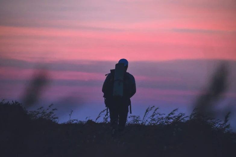 man standing in field at sunset looking down on the horizon