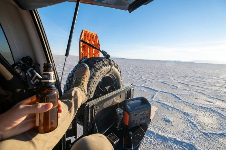 a person holding two beer bottles while sitting in a vehicle on a snowy ground