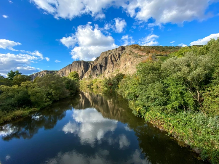 the river is reflecting a mountain landscape in the blue sky