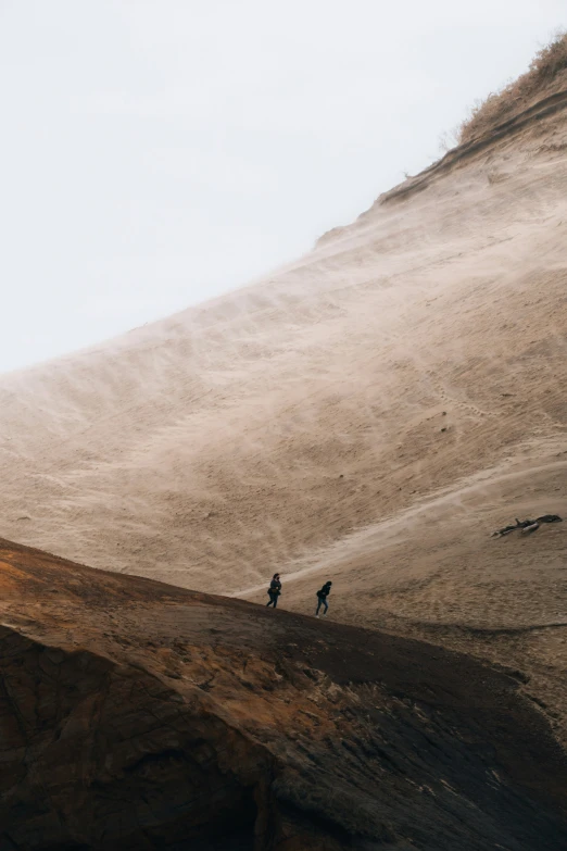 two people are standing in the sand on a hill