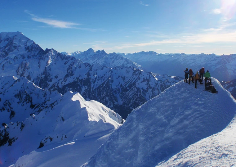 a group of skiers stand at the edge of a snow covered mountain ridge