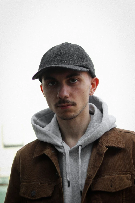 young man in brown jacket wearing cap looking off to the side