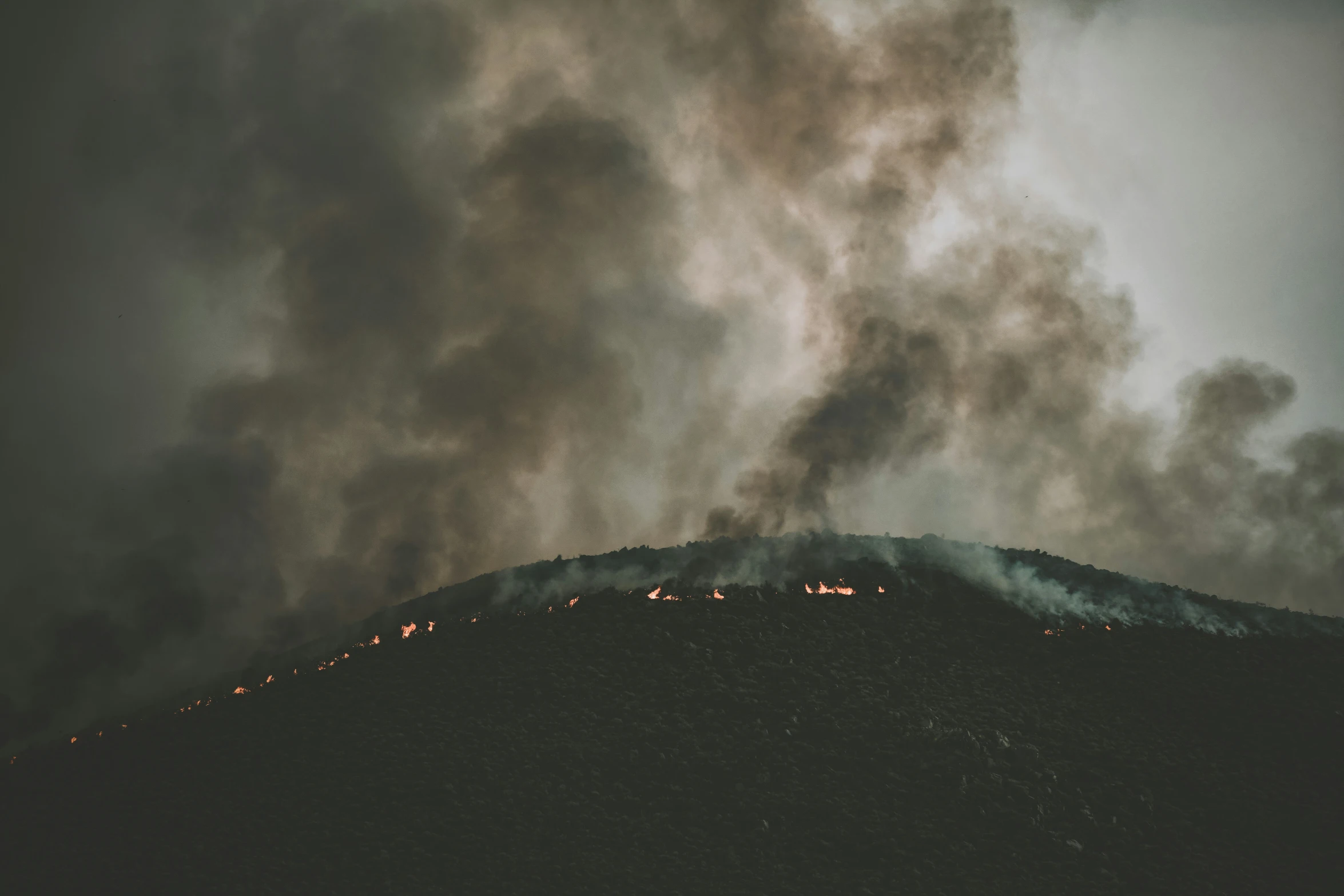 smoke coming from the top of a mountain on top of a hill