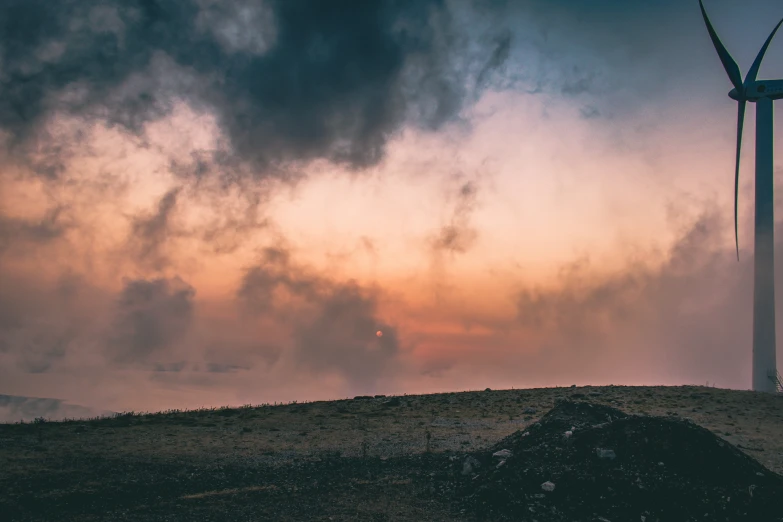 wind turbine in field with cloudy sky and sun in background