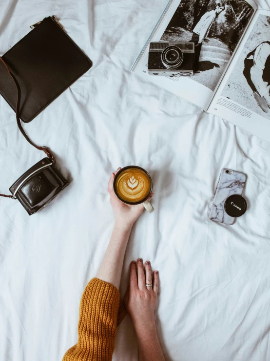 someone laying in bed with their feet up holding a cup of coffee