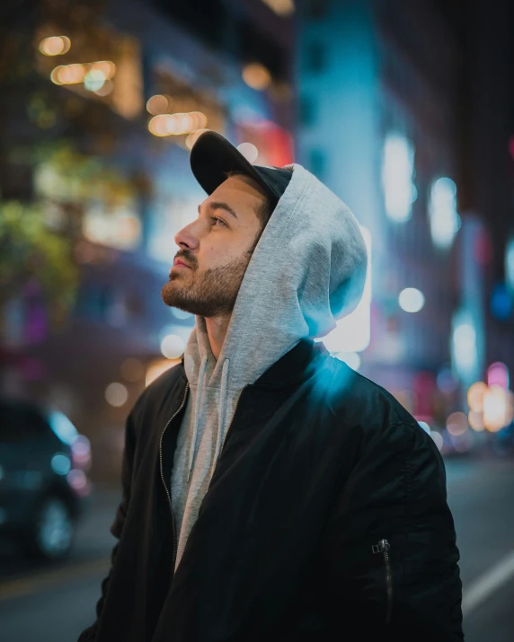 man with hoodie and hood looking ahead on city street at night