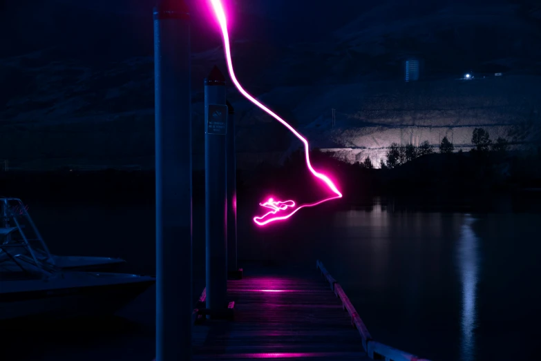 the lights of a neon pink boat are reflecting in a dark lake