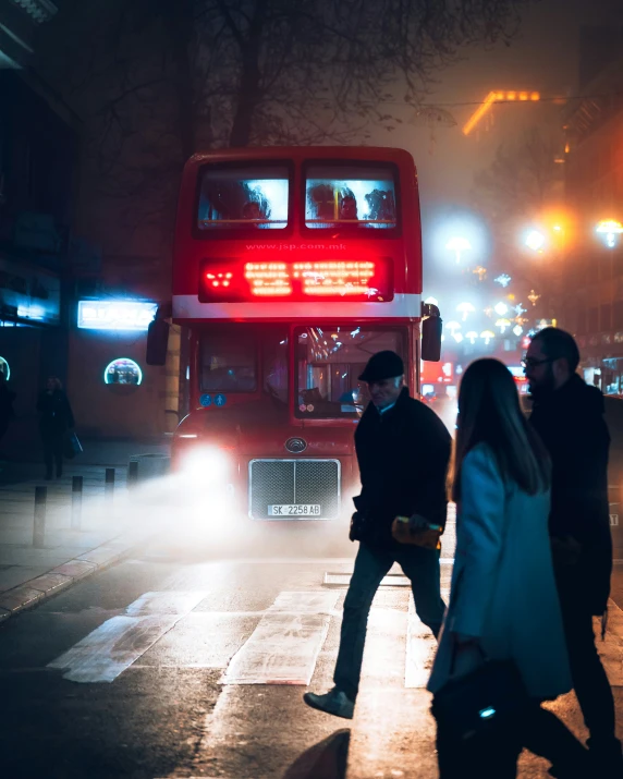 people walking in the rain at night with double decker bus in background