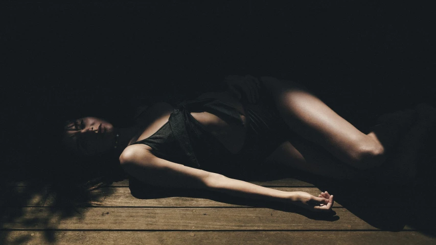 a female in a black bikini is lying on a wooden floor