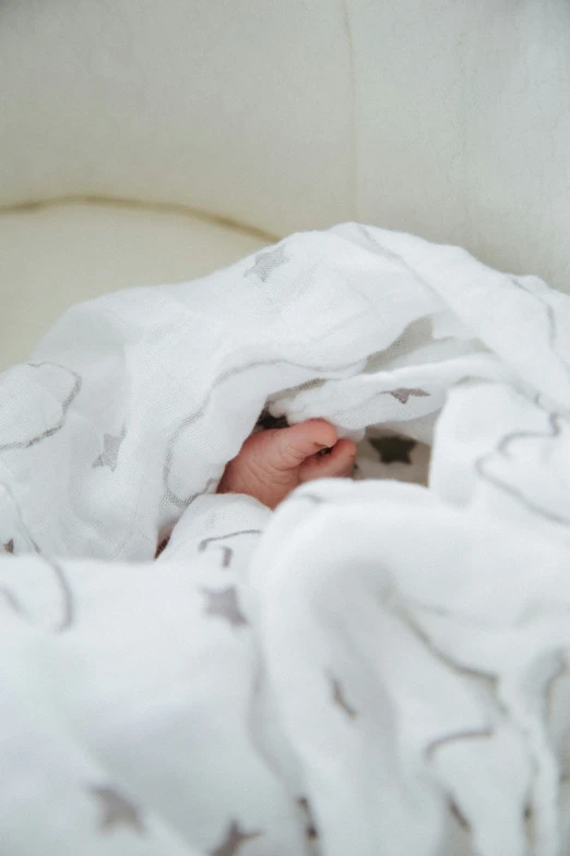 a kitten sitting under a white blanket as it hides itself in the middle of the bed