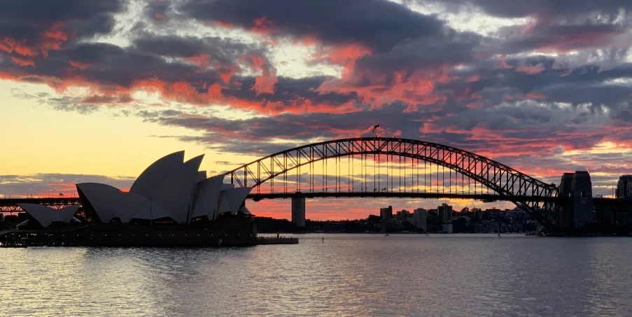 the sun sets over sydney harbour as the bridge goes over