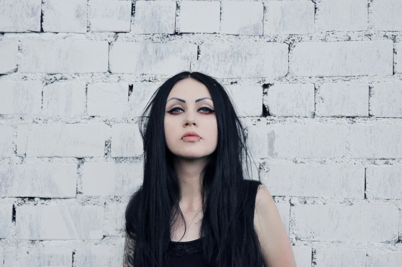 a woman with her eyes closed, leaning against a white brick wall