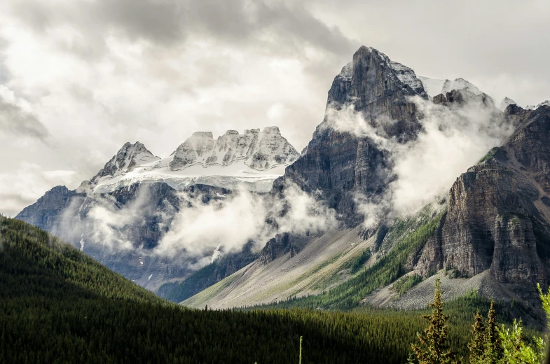 several mountain peaks with clouds and trees surrounding them