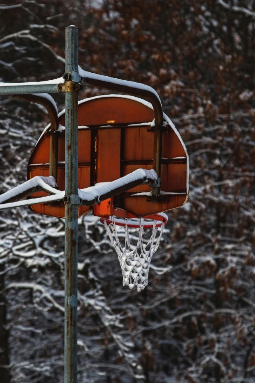 the backboard is attached to a basketball hoop and it's snowing